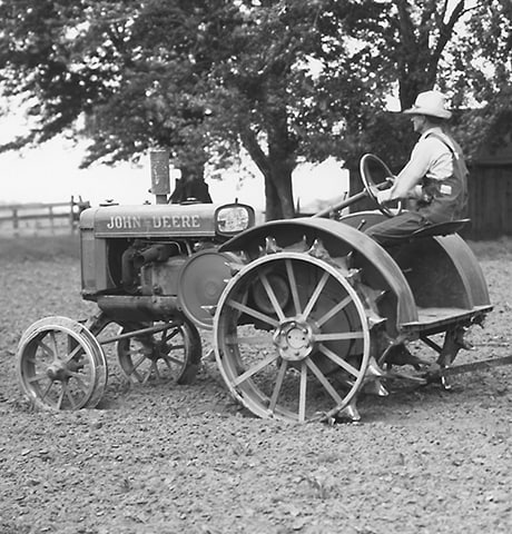 Vēsturiskais John Deere "GP" universālais traktors, kas laukā velk John Deere 7. numura rotējošās ecēšas