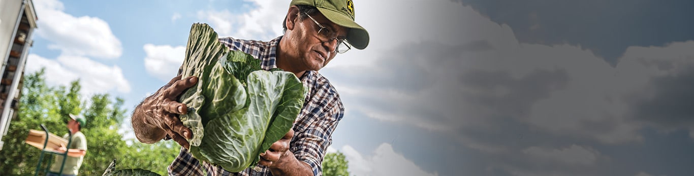 Cilvēks aizsargķiverē darba vietā ar John Deere aprīkojumu