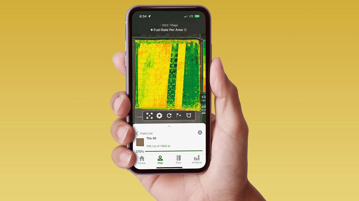 Roka, kas tur viedtālruni, parādot John Deere Operations Center ar degvielas patēriņa datiem.