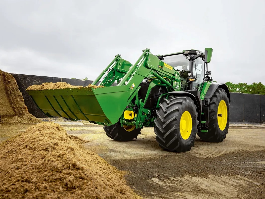 Priekšējā iekrāvēja kauss piepildīts ar skābbarību, John Deere traktoram veicot darbu ar materiālu.
