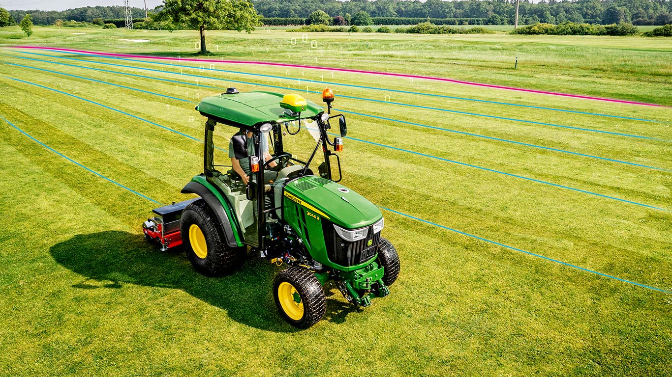 Golfa laukumu zālienu apsaimniekotājs strādā paklājzāliena zonā ar John Deere kompakto universālo traktoru.