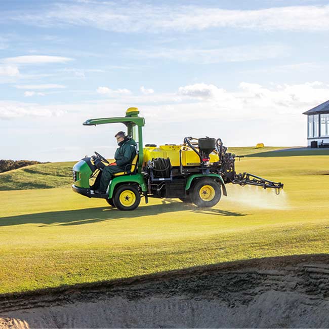 Golfa laukumu zālienu apsaimniekotājs strādā paklājzāliena zonā ar John Deere smidzinātāju