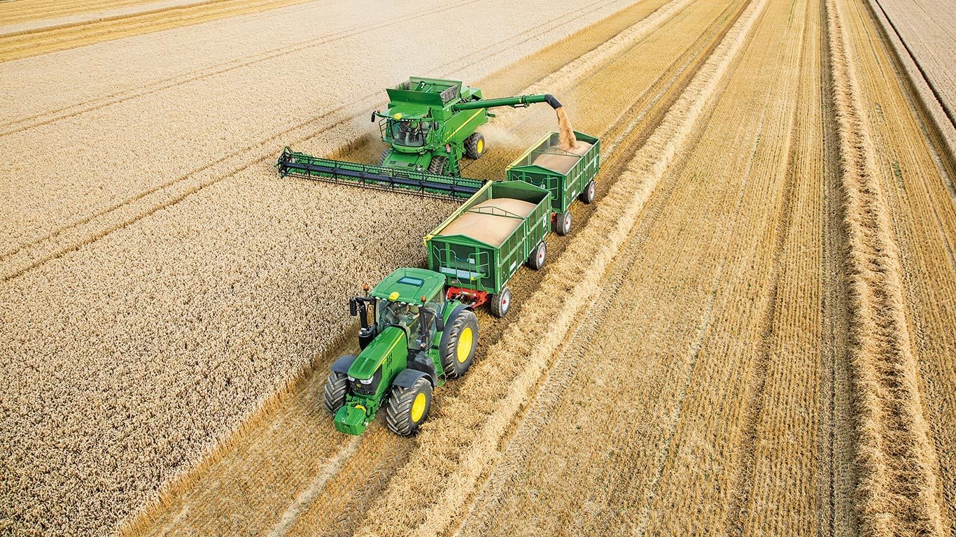 John Deere S sērijas kombains izkrauj kvie&scaron;us divkār&scaron;ā piekabē, kuru velk traktors