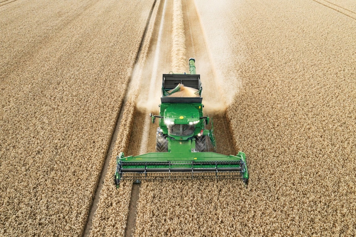 Kombains izkrauj graudus, novācot kviešus uz lauka ar hederu, kas darbojas efektīvi