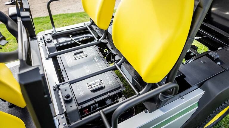 Skats no augšas uz diviem litija akumulatoru blokiem, kas uzstādīti zem spilgti dzelteniem sēdekļiem John Deere Gator GS elektriskajā universālajā transportlīdzeklī.