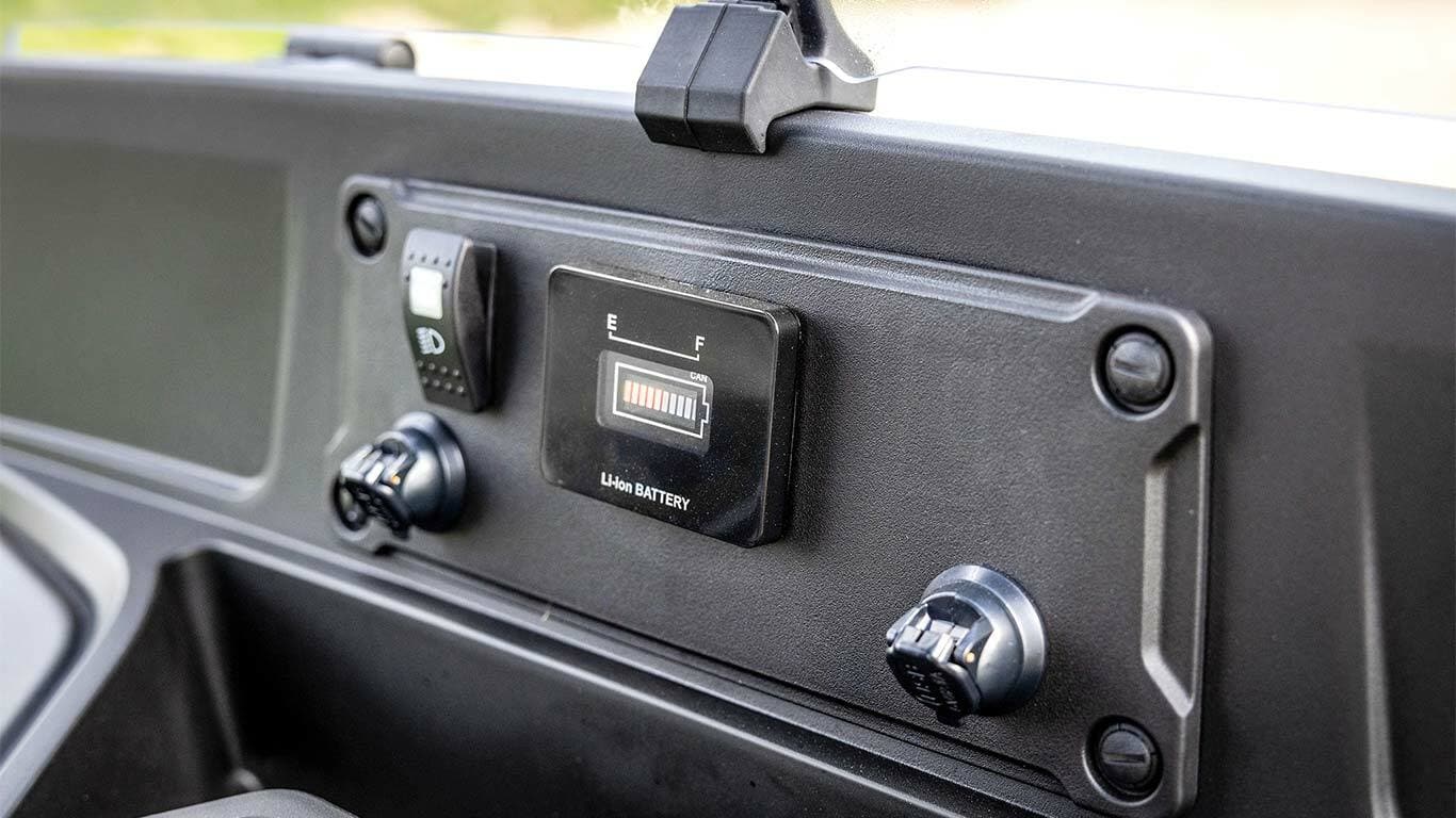 John Deere Gator GS elektriskā modeļa instrumentu panelis, kurā redzams akumulatora līmeņa indikators un strāvas pieslēgvietas.