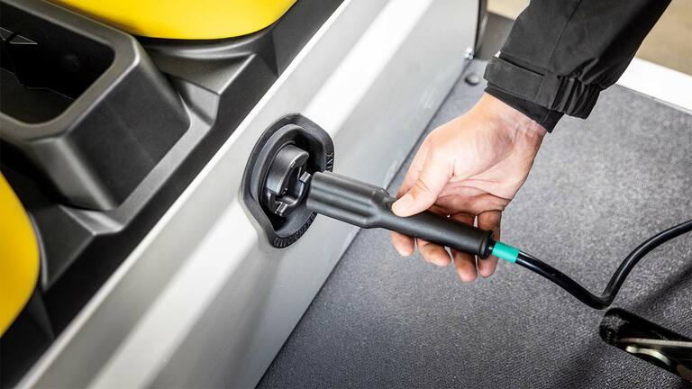 Roka, kas pieslēdz uzlādes kabeli sānu portā elektriskajā John Deere Gator GS universālajā transportlīdzeklī.