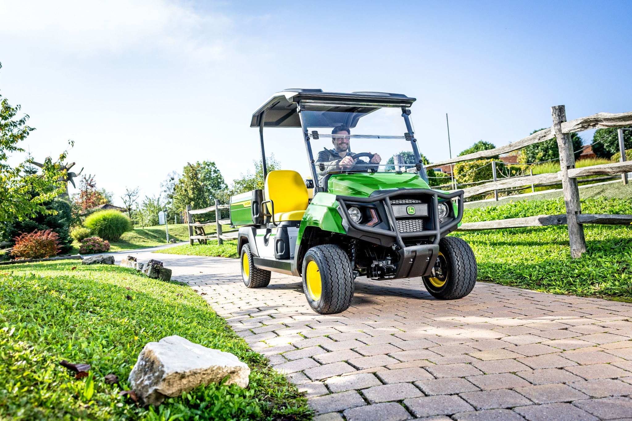 Gator GS universālais transportlīdzeklis brauc pa asfaltētu celiņu labiekārtotā teritorijā Gator GS universālais transportlīdzeklis brauc pa asfaltētu celiņu labiekārtotā teritorijā