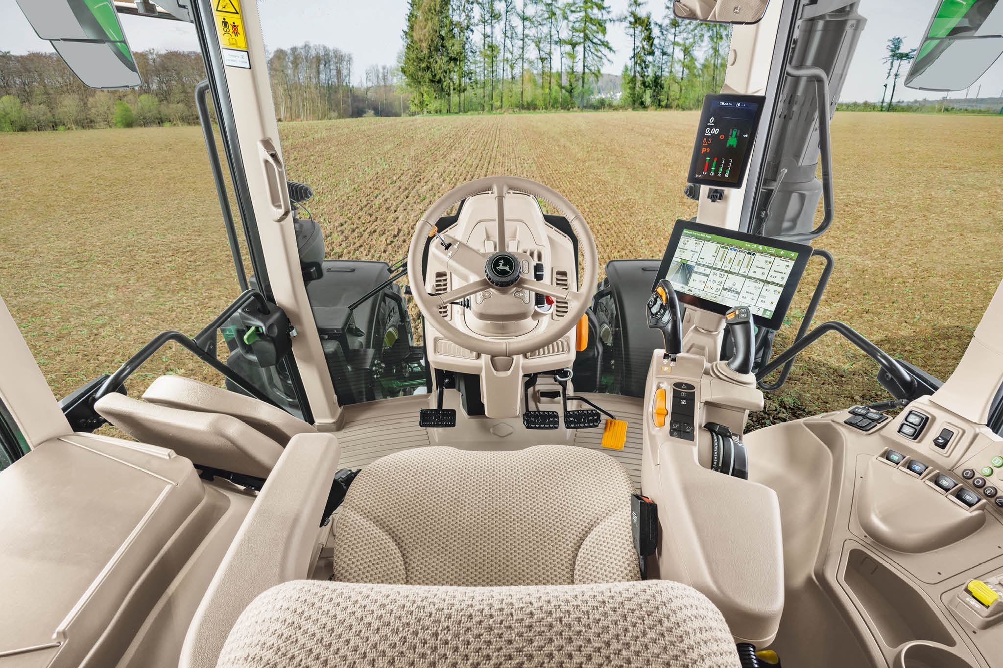 John Deere 6M sērijas traktoru kabīne ar operatora sēdekli, stūri un digitālajiem displejiem, kabīnes iekšpuses pārskats.
