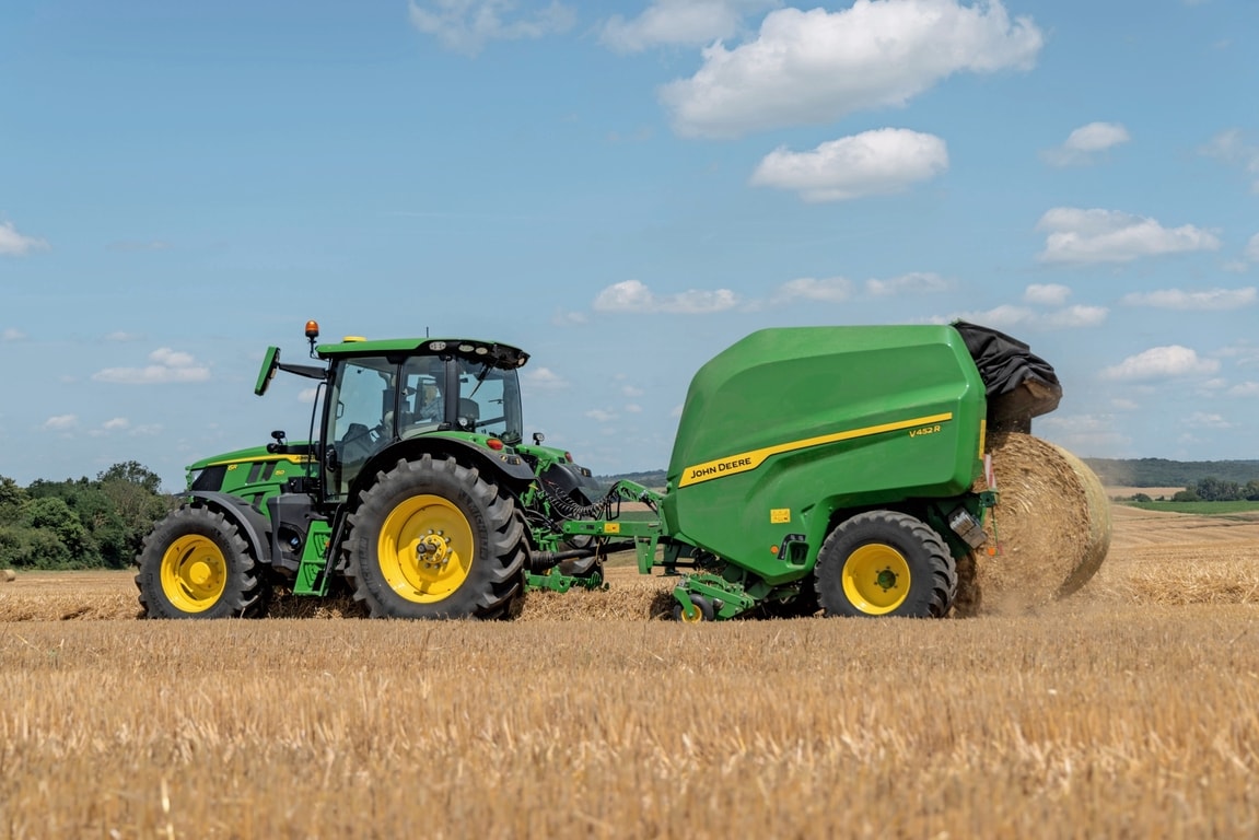 John Deere V452R uz salmu lauka, ko velk John Deere 6R 150, izstumjot rulli