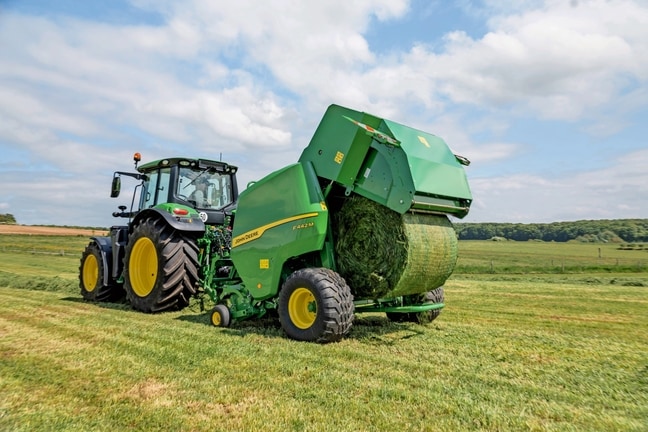 John Deere F442M presi velk John Deere 6M traktors, izstumjot zāles rulli